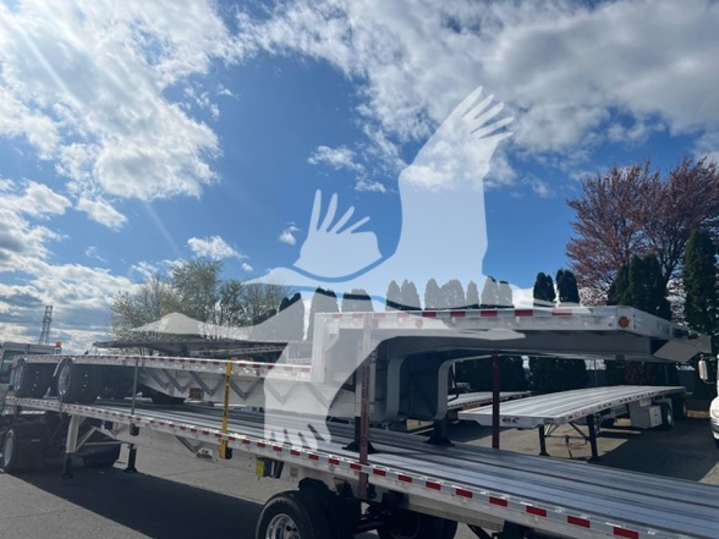 Drop deck trailer with flatbed sections and side rails, labeled Bubba Drop; white and silver with warning triangles and reflective tape.