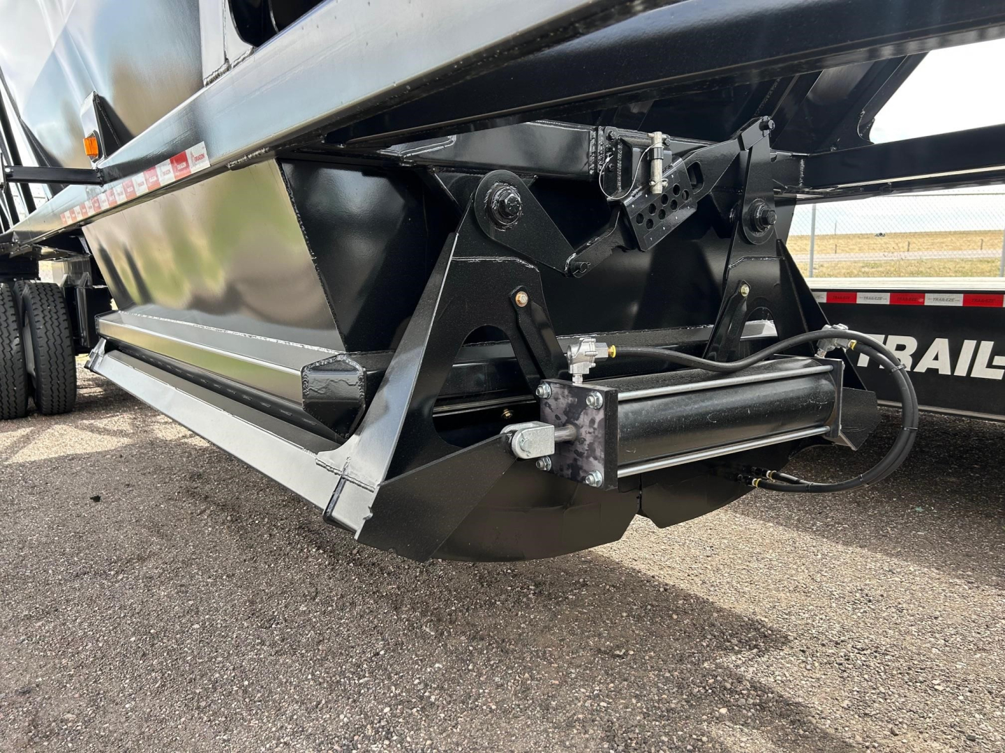 Dump trailer hitch assembly and underside of Versa Vale trailer showing hydraulic or pneumatic line routing and support brackets.