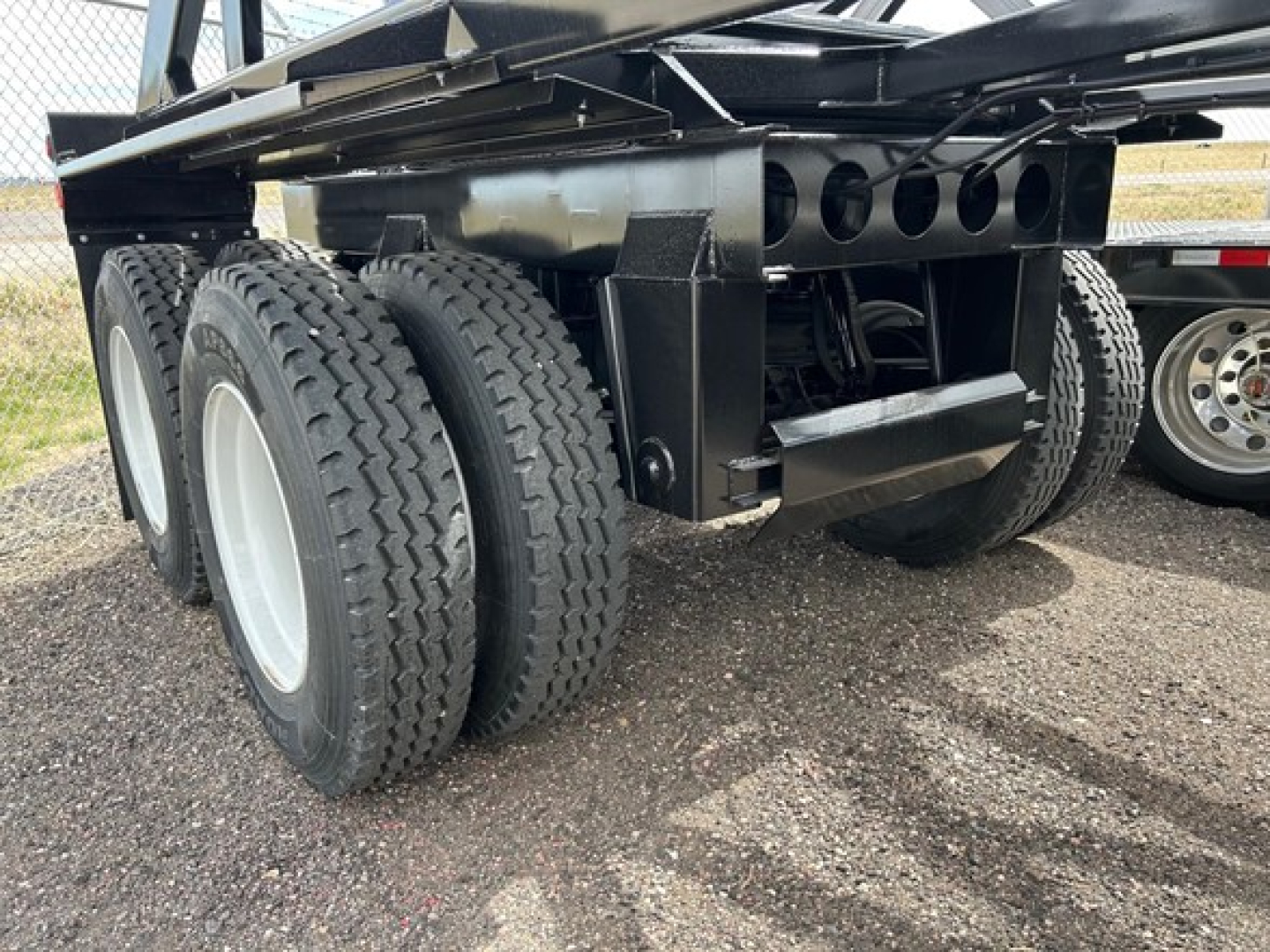 Trailer rear axle assembly showing dual rear tires and black metal frame with mounting brackets; no legible serials visible in this view.