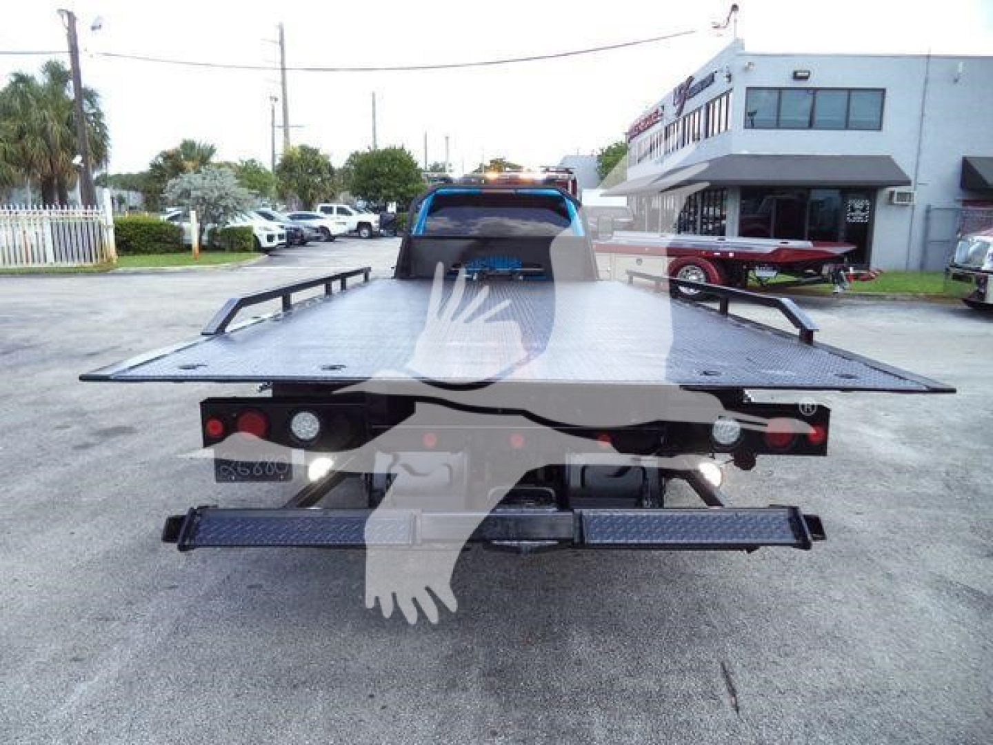 Rear view of a flatbed tow truck with platform; license plate area; taillights; bumper steps; license plate frame; overhead truck scene.