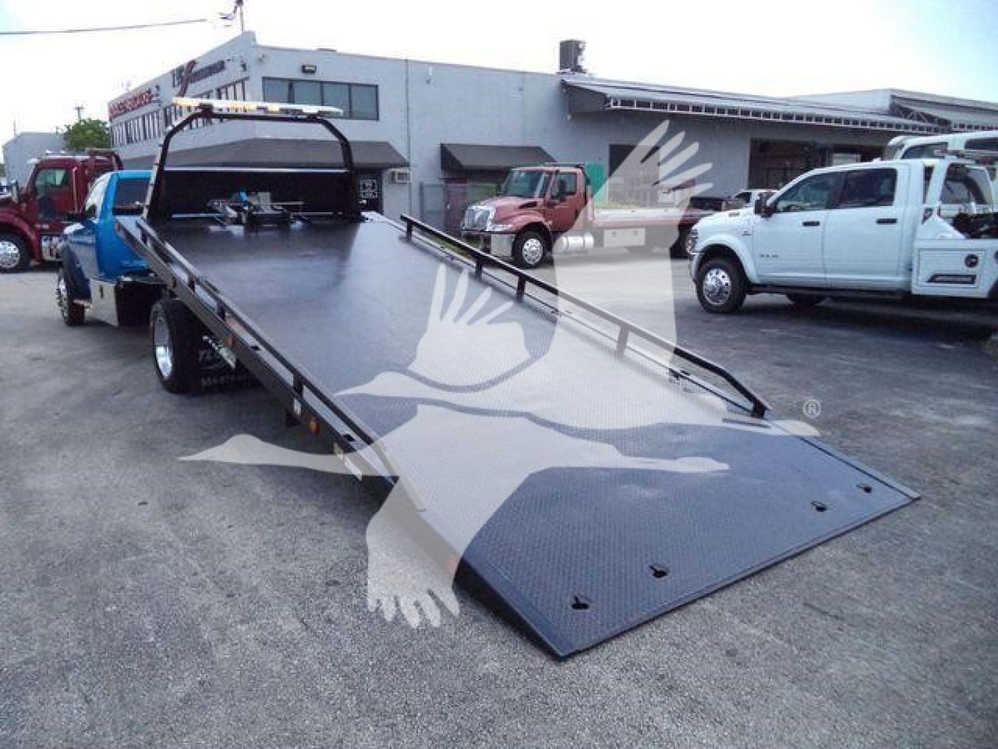 Ram 5500 rollback truck flatbed with extended loading ramp in a truck yard, showing a black steel bed and loading ramps.