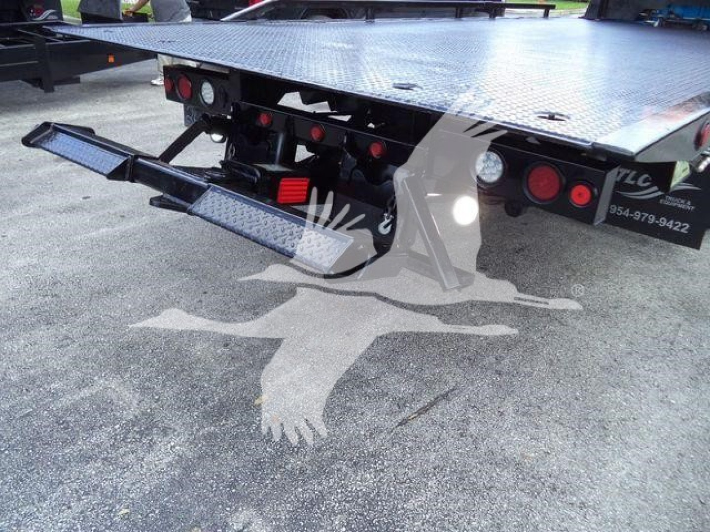 Ram 5500 rollback tow truck bed rear with hydraulic lift and safety lights. Platform steel deck with textured surface and rear step / bumper. Visible taillights and reflective markings.