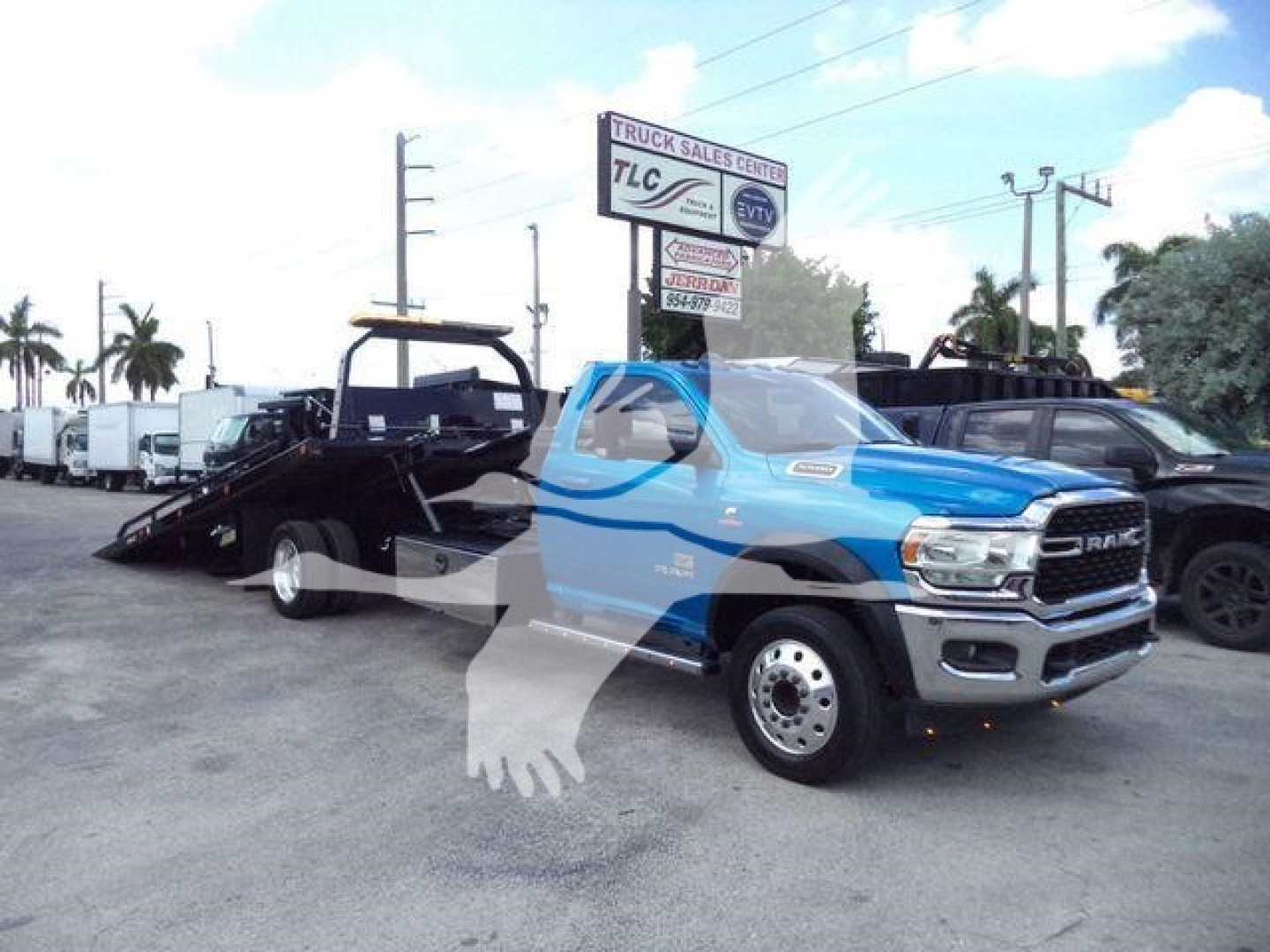 Ram 5500 SLT pickup truck with rollback tow bed attached, blue cab and gray front, parking lot background, side view showing front grille and wheel
