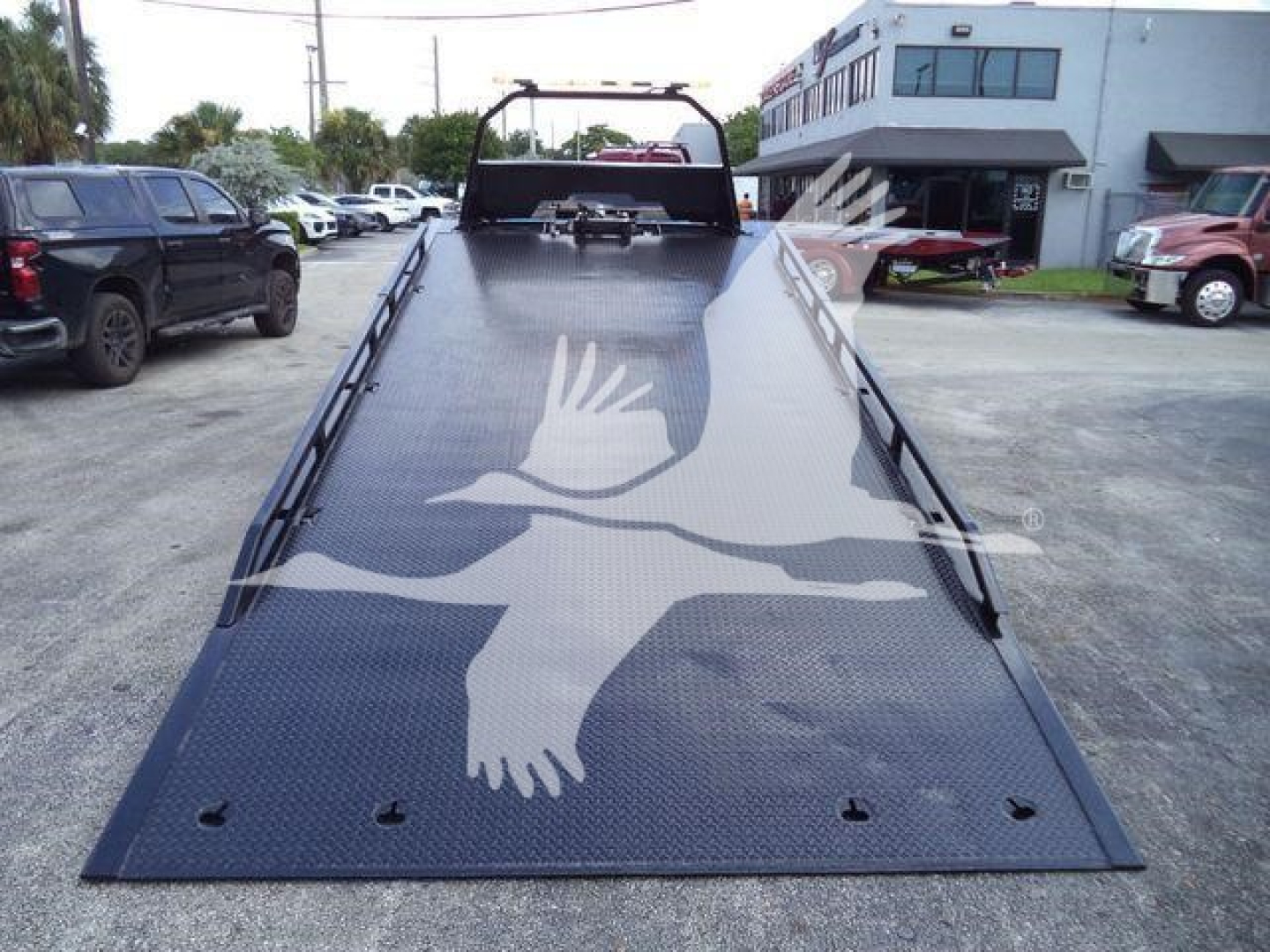 Truck bed tilt tow truck with hydraulic ramp showing a large white bird graphic and diamond plate surface.