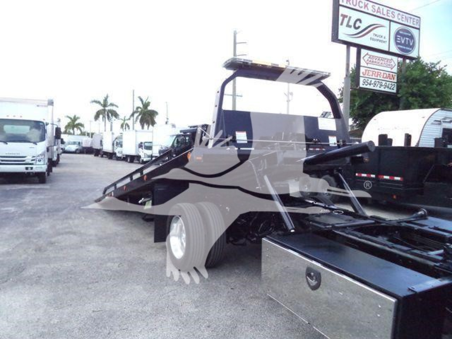 Ram 5500 rollback tow truck in a dealership lot with loading ramp and flatbed, partial front cab visible.