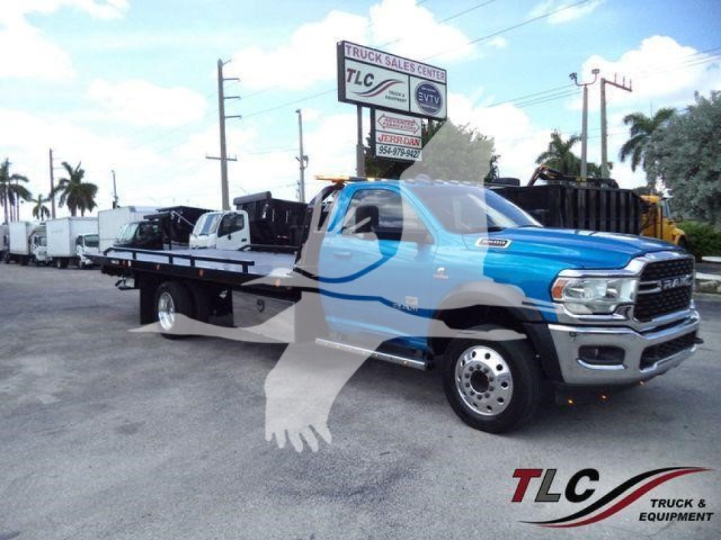 Ram 5500 tow truck in yard with rollback bed and DuraRide dual rear wheels visible, front grille and cab badge readable, TLC Truck Sales Center sign in background.