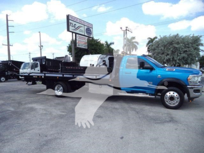Ram 5500 rollback truck in blue and white, extended cab, long flatbed with wheel-lift equipment, dealership lot in background.