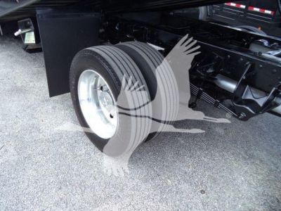Truck chassis with dual rear wheels and visible suspension in front of wheel well. Flatbed/rollback setup with tire and rim. Partial undercarriage components visible.