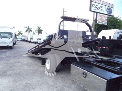 Ram 5500 rollback tow truck in a dealership lot with loading ramp and flatbed, partial front cab visible.