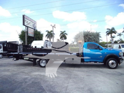 Ram 5500 tow truck with rollback bed and blue cab, side view in dealership lot.