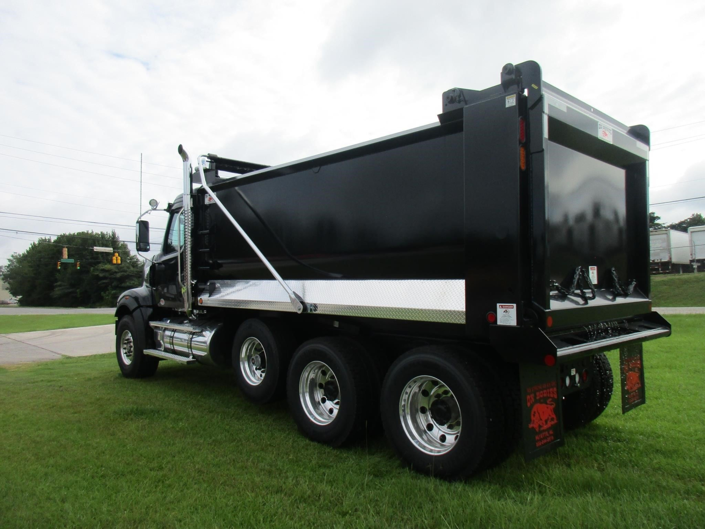 Western Star dump truck in service position showing black dump body, rear tailgate, side rails, and triple rear axles with chrome wheels.