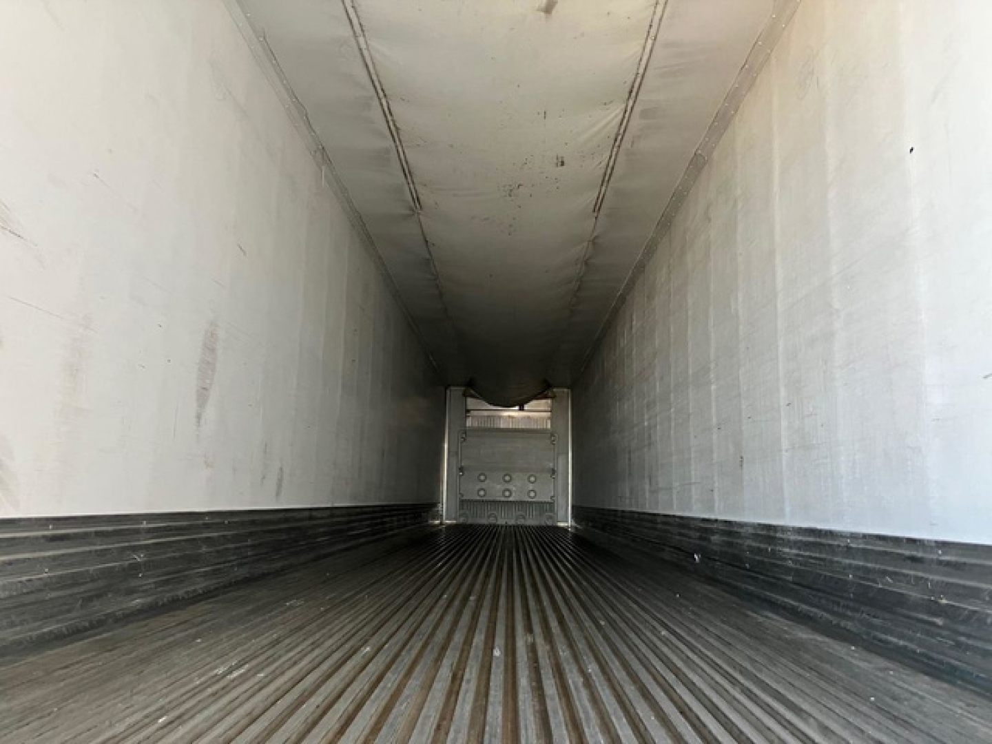 Reefer trailer interior viewed from back toward front showing long cargo bay with ribbed floor and white side walls.