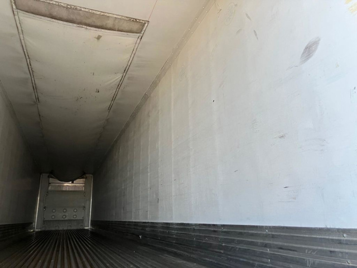 Reefer trailer interior with white walls and ribbed floor, open at rear showing trailer end cap.