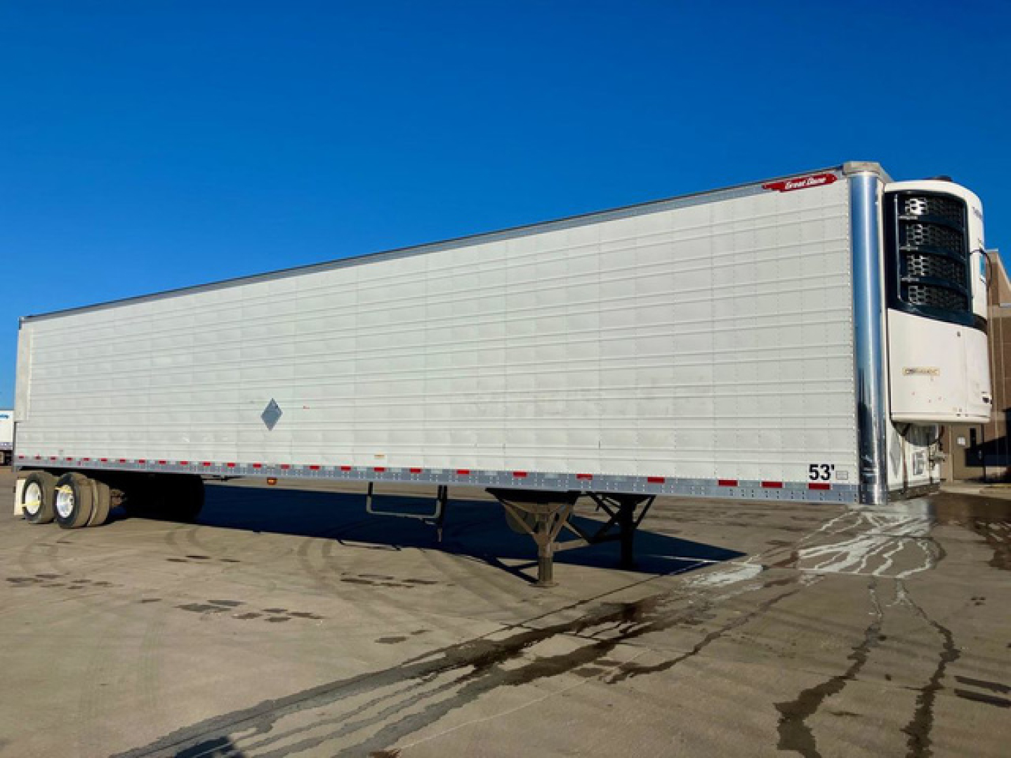 Great Dane reefer trailer with white insulated body and refrigeration unit at front, side view, 53' length, docked on wet pavement.