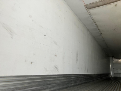 Trailer interior wall and floor of a refrigerated Great Dane reefer trailer, metal ribbed floor and white wall with scuff marks.