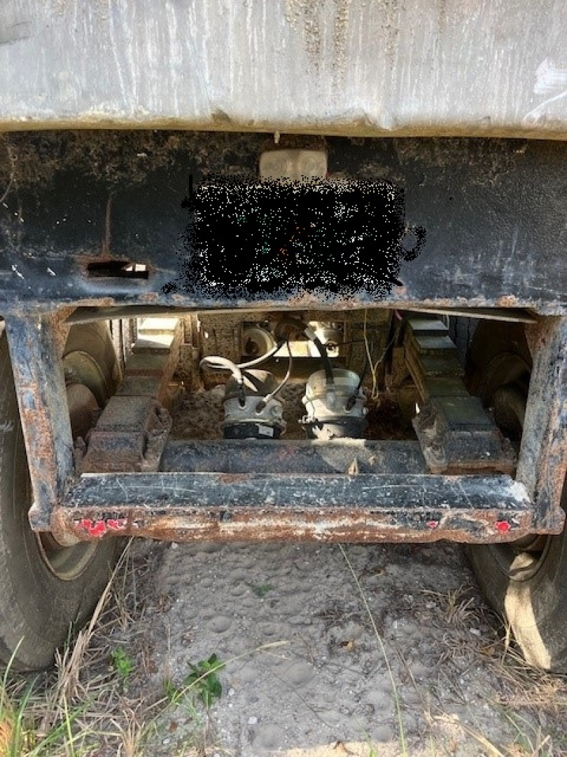 Trailer undercarriage showing rear suspension and landing gear on a dump trailer; lower frame with wheels and mechanical components visible.