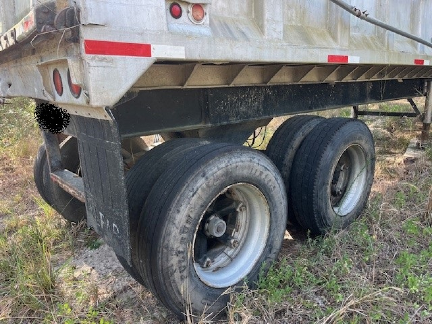 Trailer rear showing dual axles and tires under a dump trailer, with metal frame and wheel wells visible.