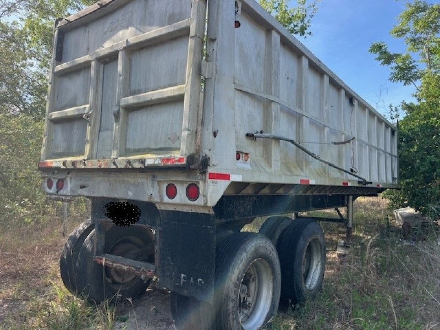 Dump trailer rear view showing dual rear axles, metal dumping bed, weathered aluminum walls with rear doors.