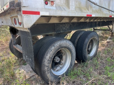 Trailer rear showing dual axles and tires under a dump trailer, with metal frame and wheel wells visible.