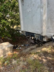 Dump trailer rear corner showing hitch and suspension components under a silver aluminum body.