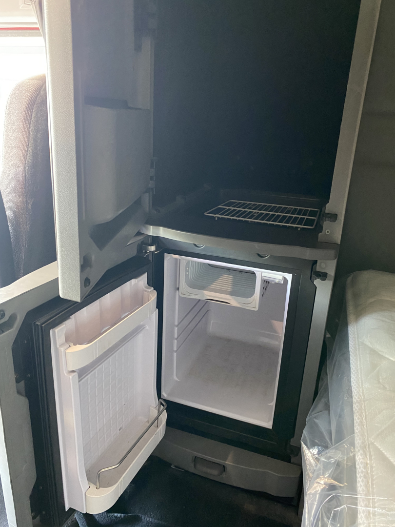 Truck cab fridge and small freezer compartment with open doors in a Peterbilt 567 sleeper, showing compact fridge/freezer with shelves and freezer drawer.