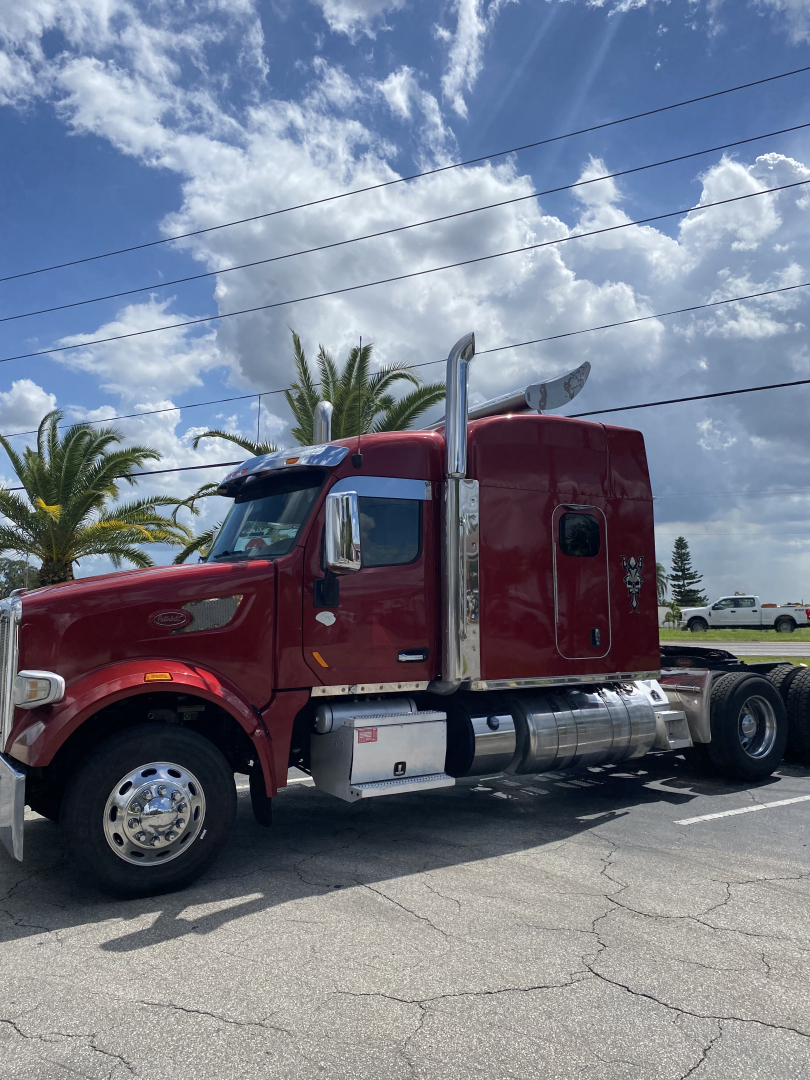 Side view of a red 2015 Peterbilt 567 conventional sleeper tractor showing chrome exhaust stacks and fuel tanks.