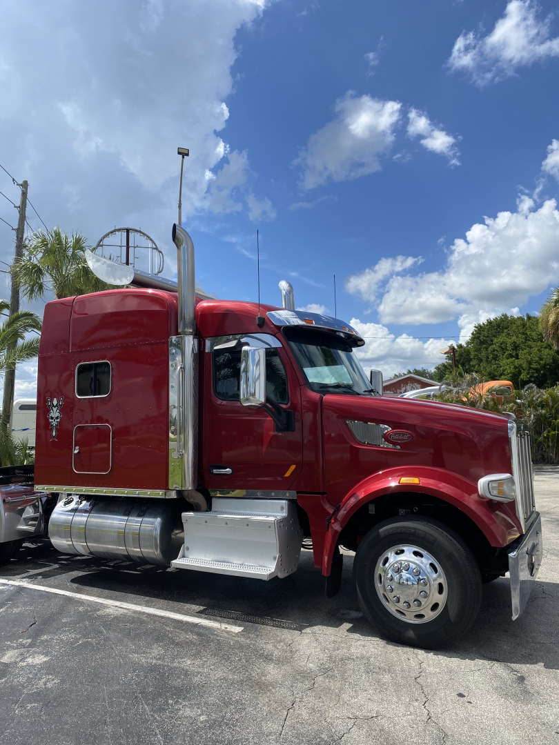 Peterbilt 567 conventional sleeper truck in red, side view showing cab, chrome fuel tanks, and exhaust stacks.