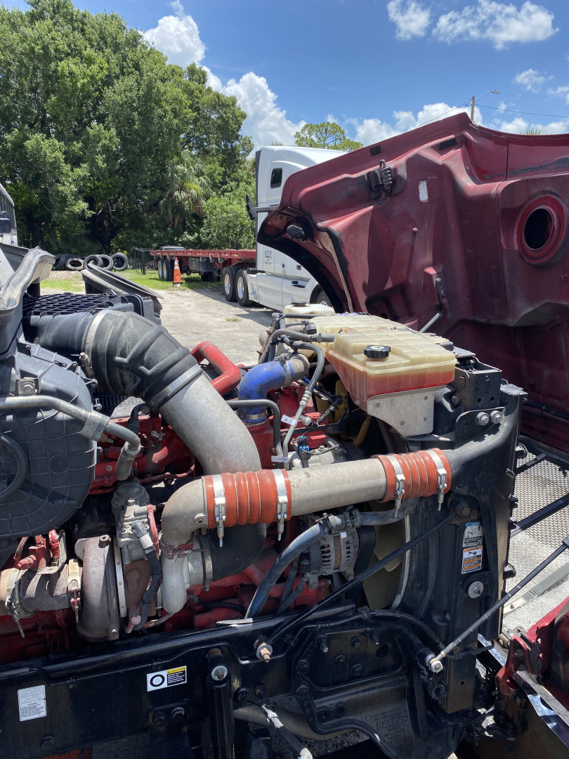 Peterbilt 567 engine bay showing coolant reservoir, hoses, and various engine components.