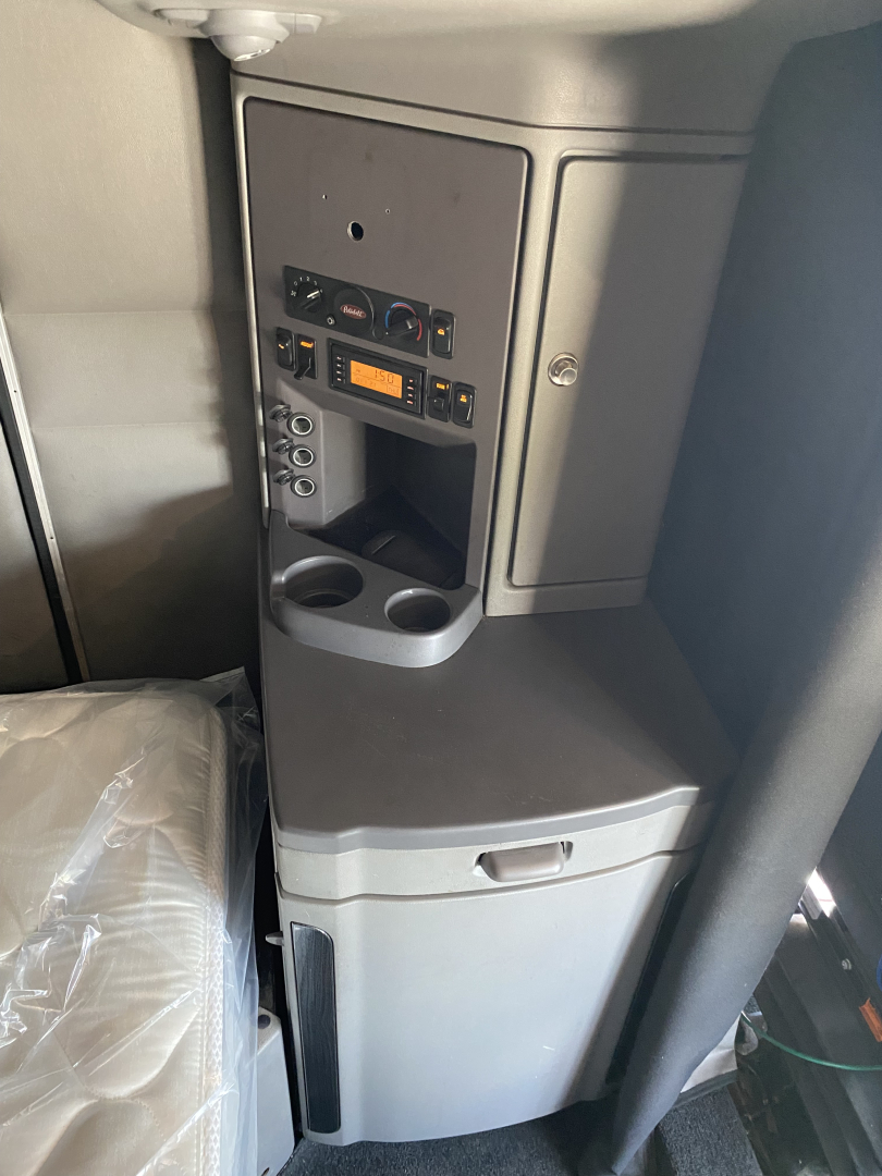 Interior sleeper cab center console with control panel, cup holders, and storage drawers in a 2015 Peterbilt 567, showing switches and a small orange display.