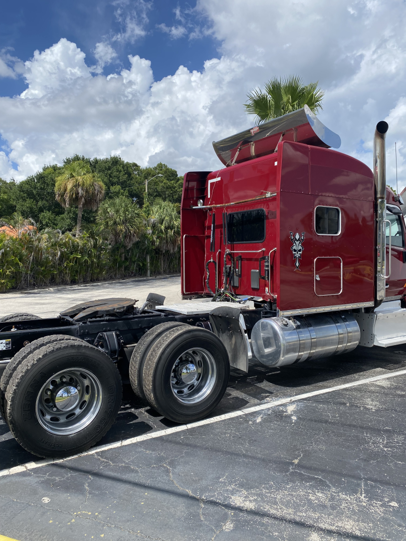 Peterbilt 567 tractor cab side view in red, with chrome fuel tanks and dual rear axles.