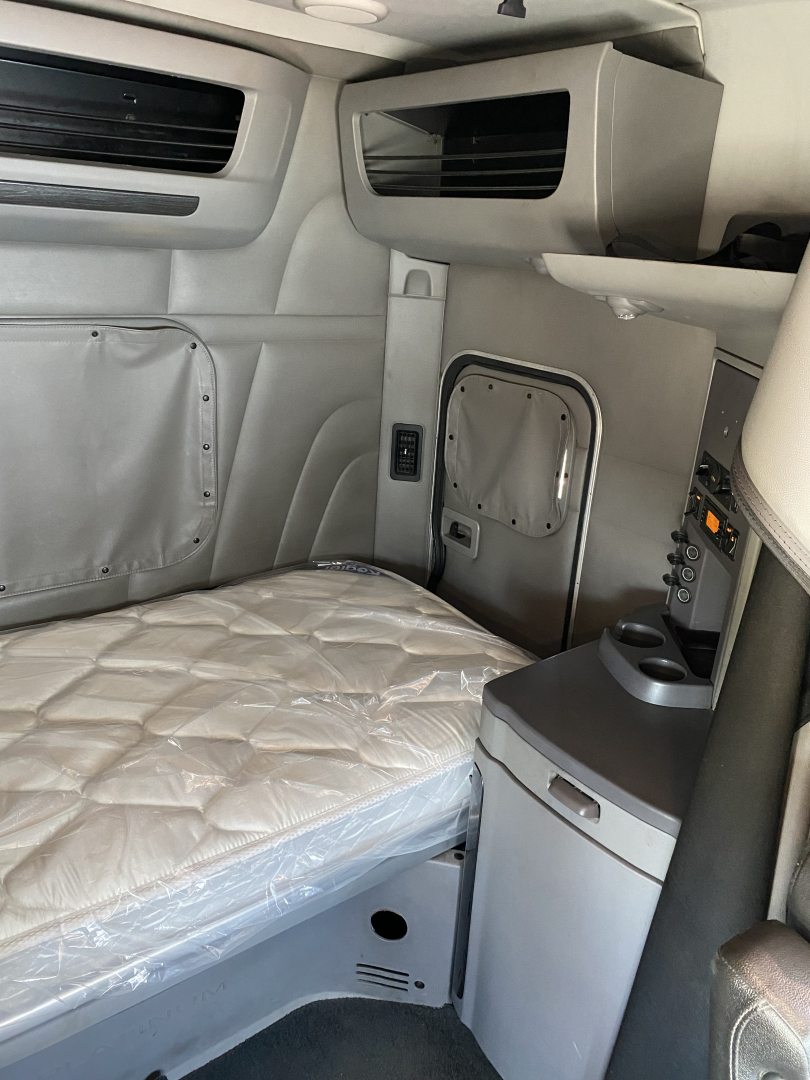Truck cab interior of a 2015 Peterbilt 567 showing sleeper bed with quilted mattress, side panel, storage compartments, and dashboard area.