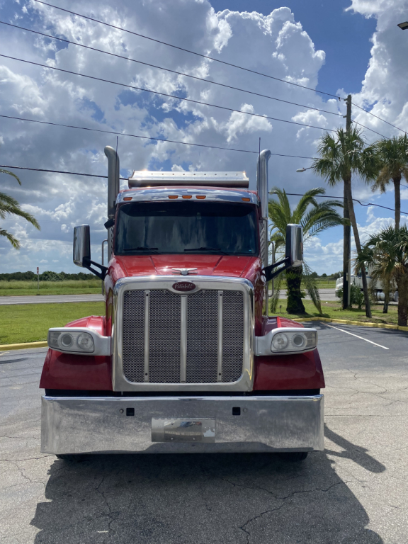 Peterbilt 567 truck front view with large chrome grille and red cab in a lot.
