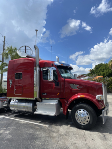 Peterbilt 567 conventional sleeper truck in red, side view showing cab, chrome fuel tanks, and exhaust stacks.