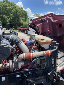 Peterbilt 567 engine bay showing coolant reservoir, hoses, and various engine components.