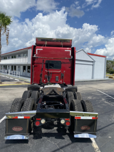 Peterbilt 567 tractor rear view showing dual rear axles, mudflaps with Peterbilt logos, and chrome bumper steps.