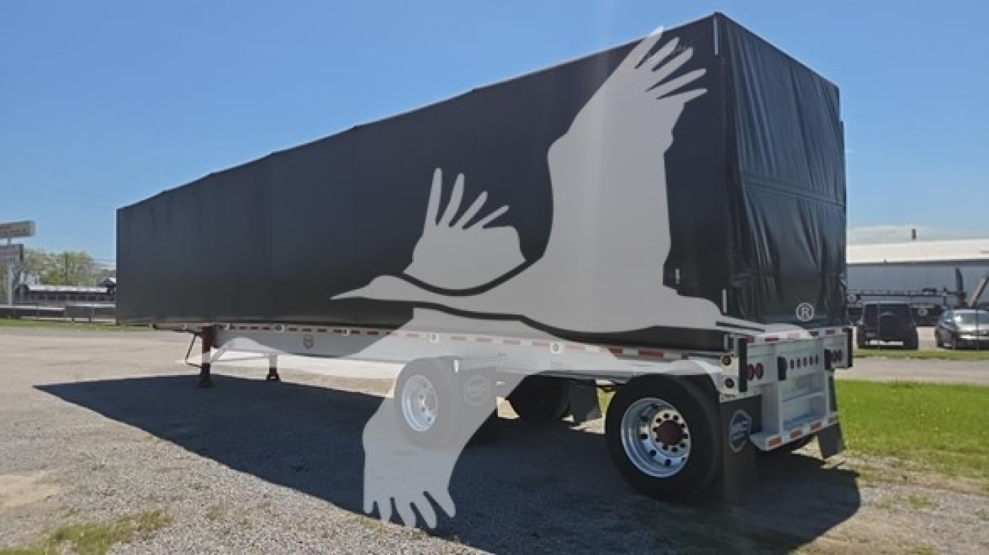 Curtainside trailer showing large white crane-like graphics on black tarp and aluminum undercarriage with dual rear wheels.