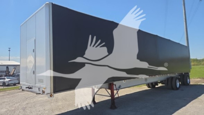 Curtainside trailer with large white bird graphic on dark gray side, tandem axle, front landing legs visible.