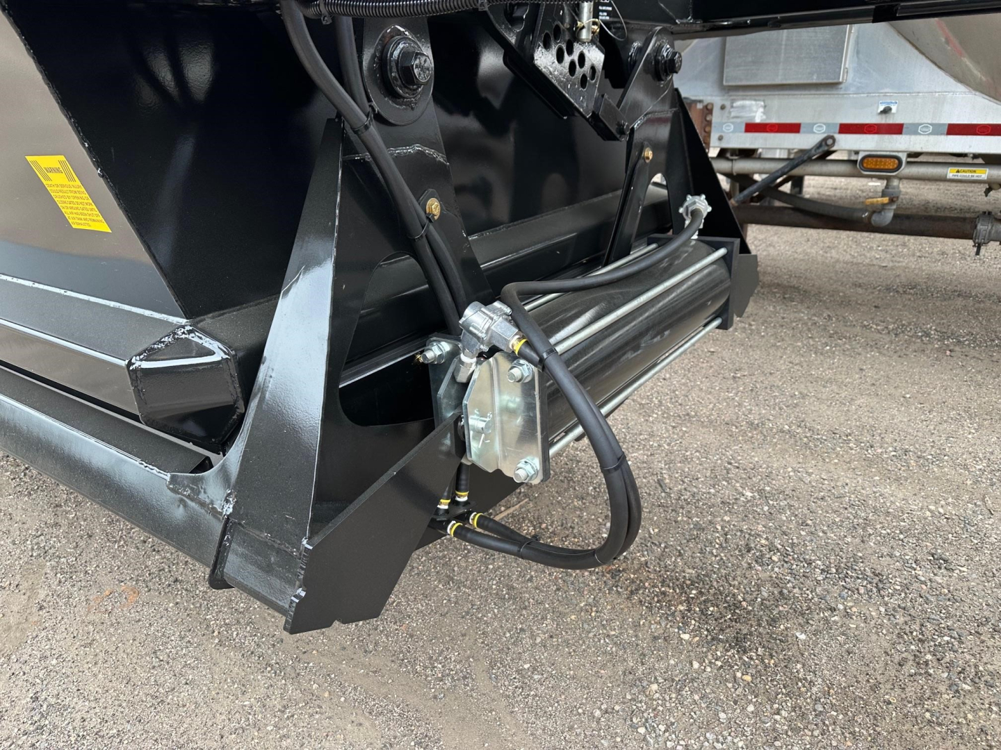 Dump trailer hitch area showing hydraulic component and attachment hose on black steel frame