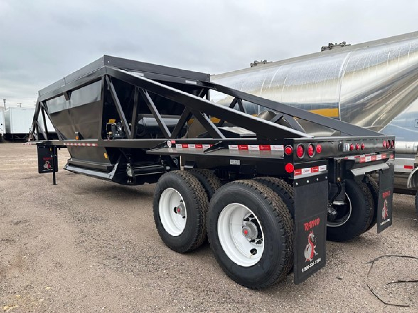 Ranco LW21-40 dump trailer showing dual axle with white rims and black frame, rear mudflaps and red/white reflective tape along sides.