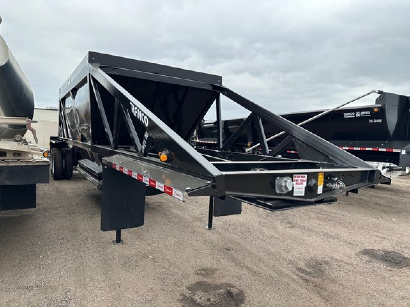 Ranco LW21-40 dump trailer showing steel frame, black paint, side rails, and landing gear in a parking lot.