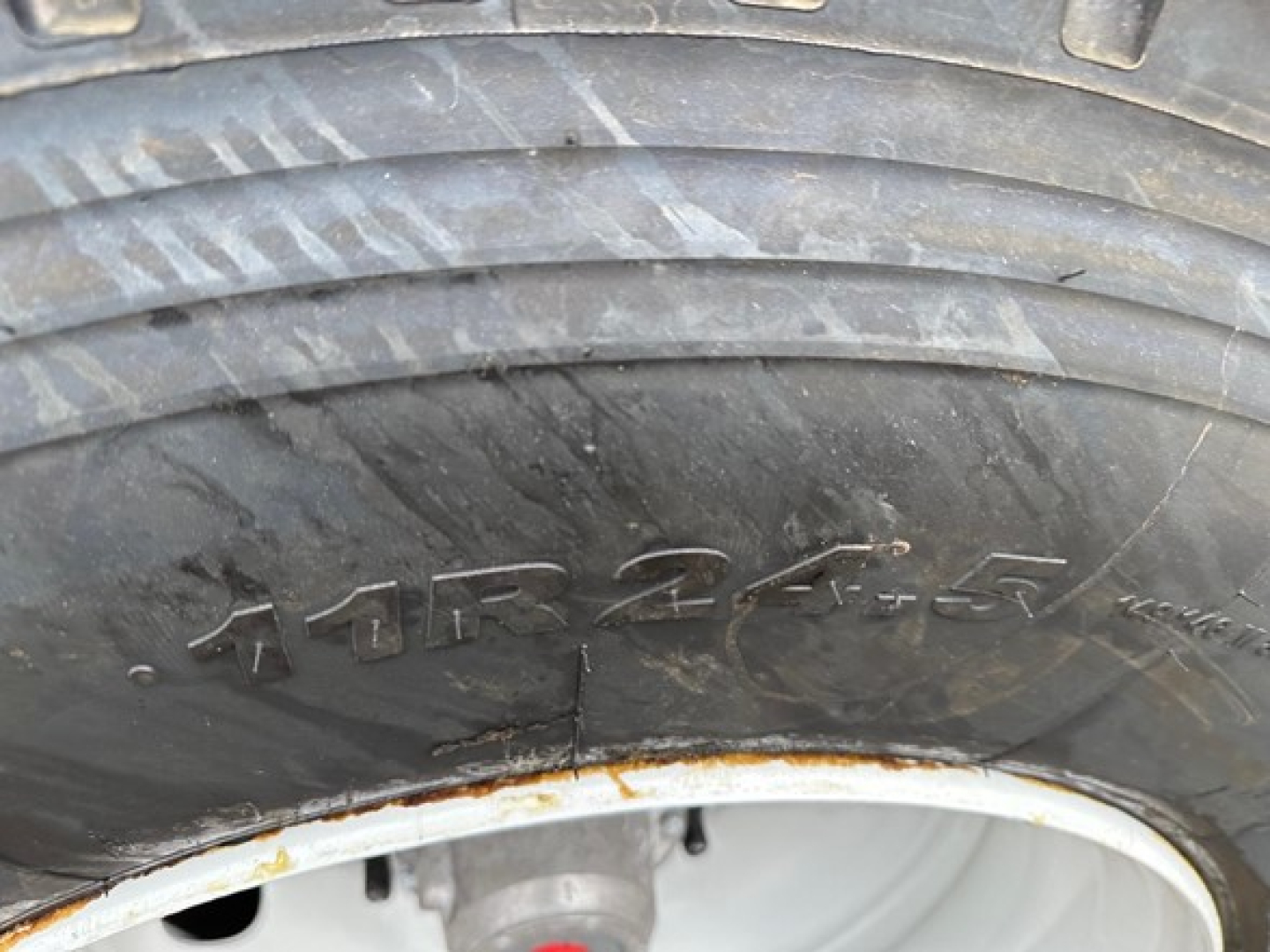 Tire sidewall with worn tread and a ridge crack; portion of wheel showing rim and tire markings.