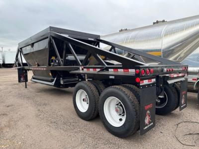 Dump trailer with black framework and white wheels, showing 'Ranco' branding on mud flaps and hex truss structure; rear dual axle setup visible.
