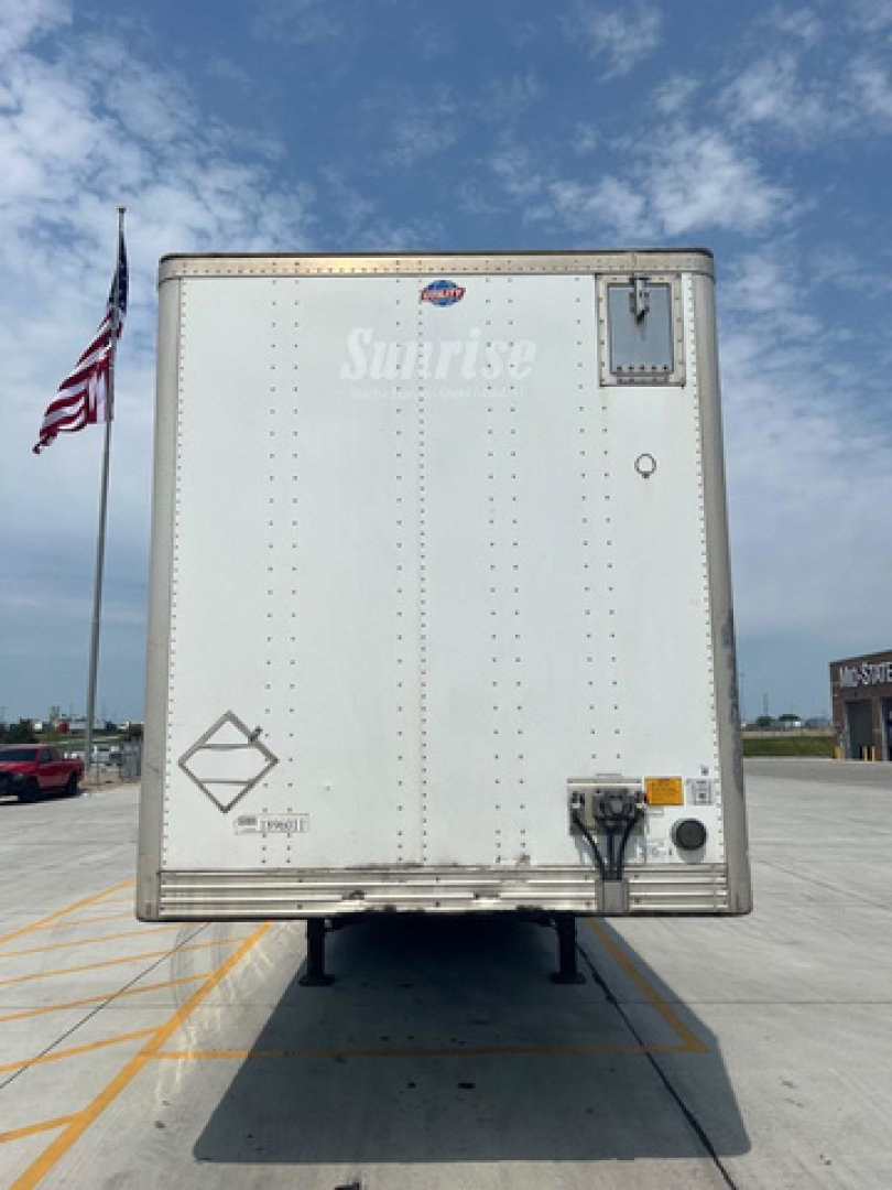 Trailer rear view showing metal cargo box with Sundowner logo, safety placards, and rear hitch assembly.