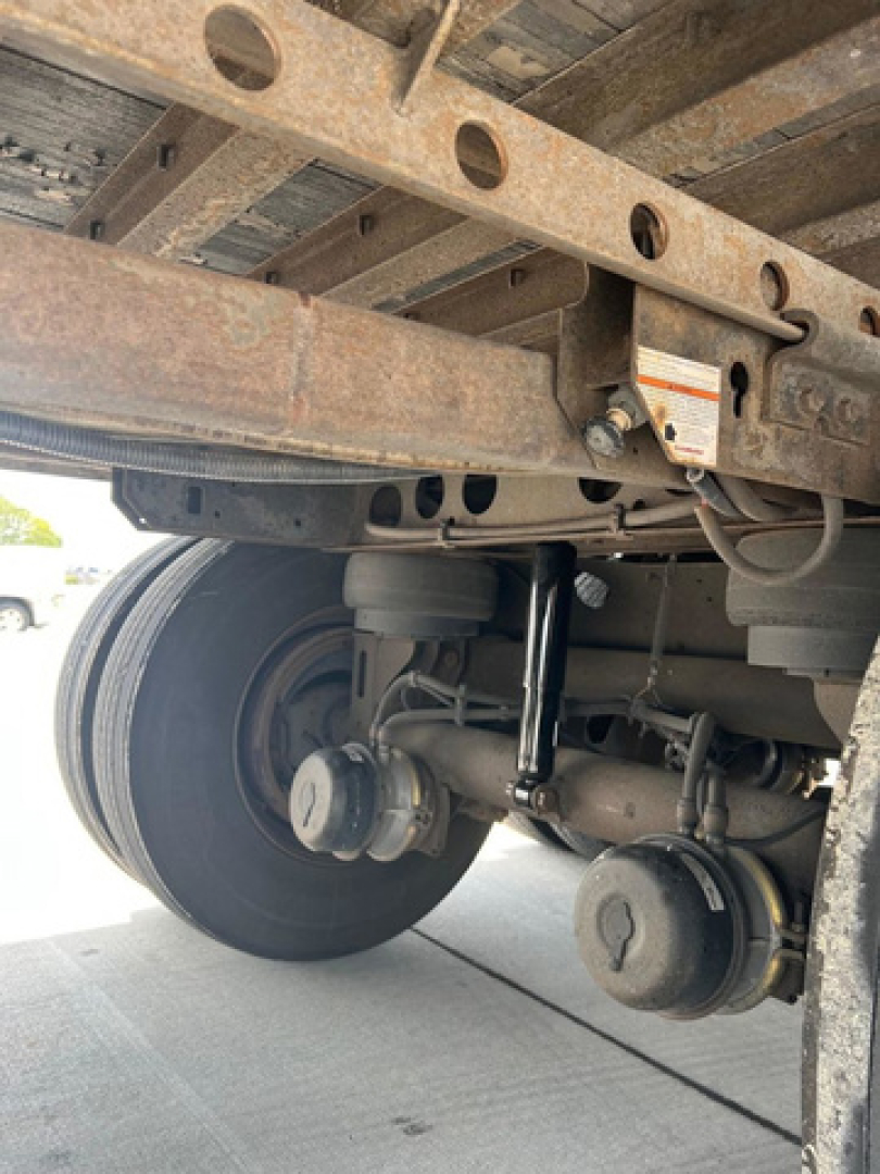 Underbody view of a 2012 utility van showing suspension components, leaf springs, axle, and wheel hub. Rust appears on frame rail and structural members.