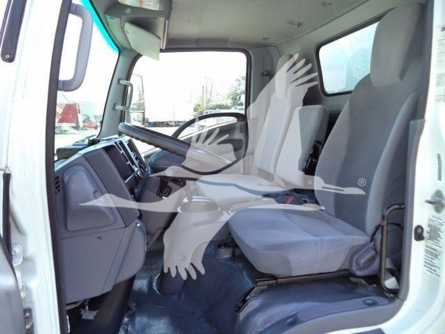 Isuzu NPR/NRR cab interior showing steering wheel and driver seat, dashboard, and front passenger seat; light gray seats.