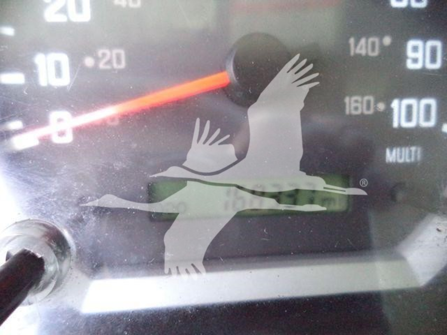 Dashboard gauge cluster showing speedometer and temperature dials with reflection of a logo. No specific model text visible.