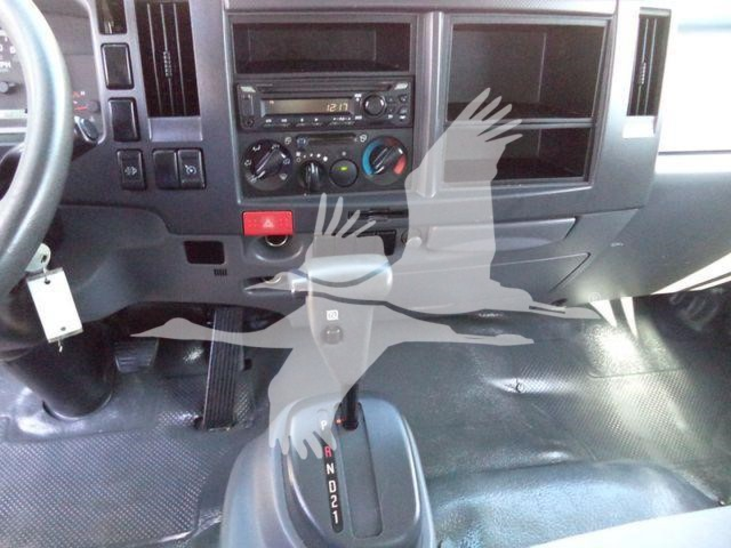 Isuzu NPR/Nrr dashboard and gear selector area showing center console with climate controls and radio; transmission shifter in view with gears P R N D 2 1.