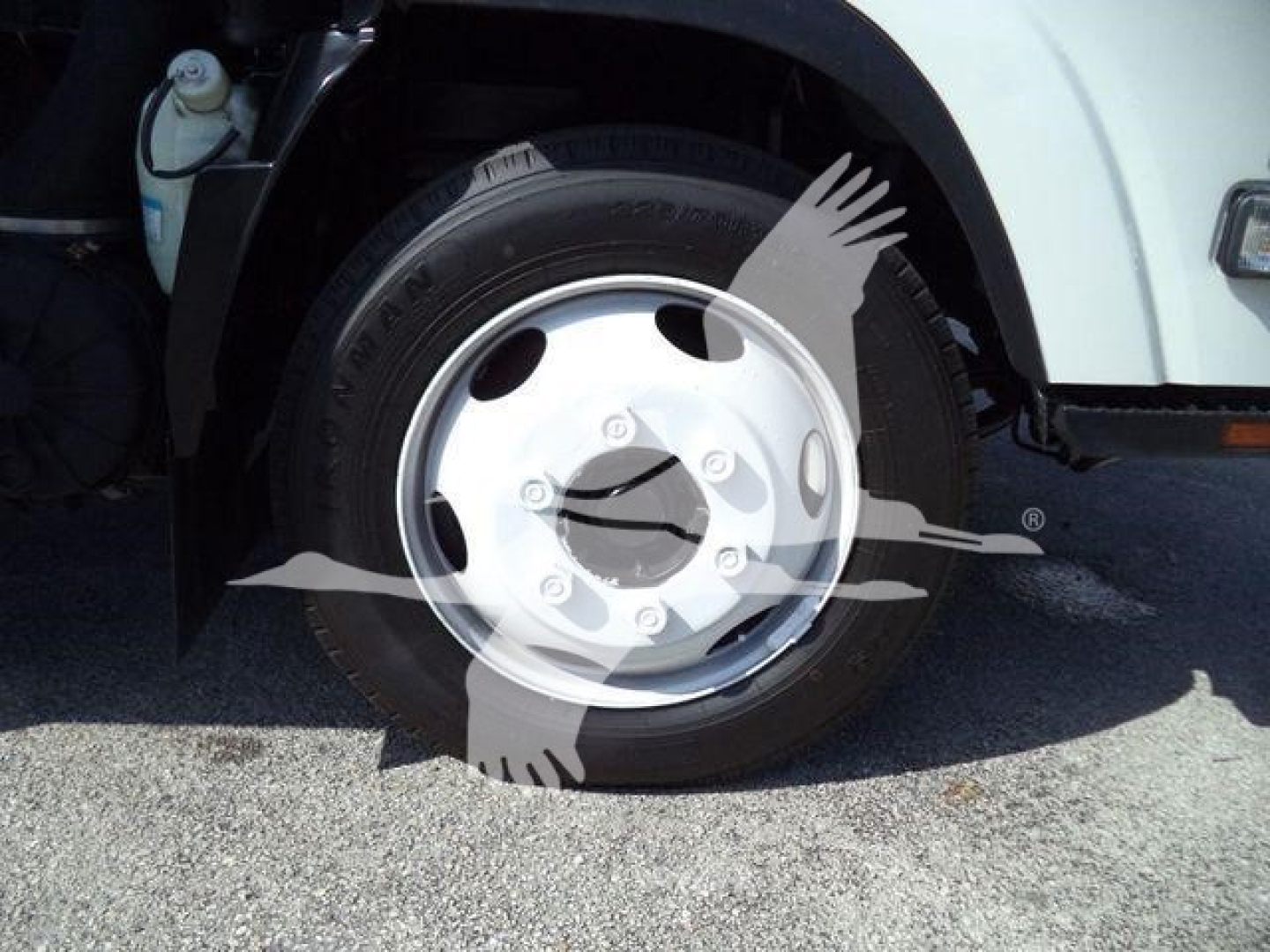 Isuzu NPR front wheel well and tire showing steel wheel with five lug nuts and hubcap; cab edge and wheel well with a coolant reservoir visible.
