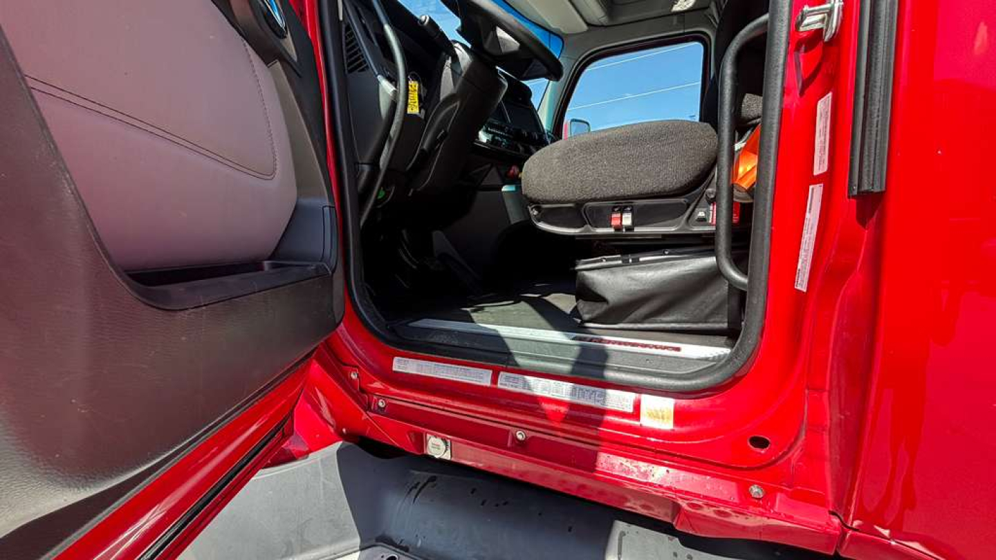 Kenworth cab interior of a 2022 T680 showing driver seat and door sill area, red exterior, open door, steering wheel, and dashboard visible.