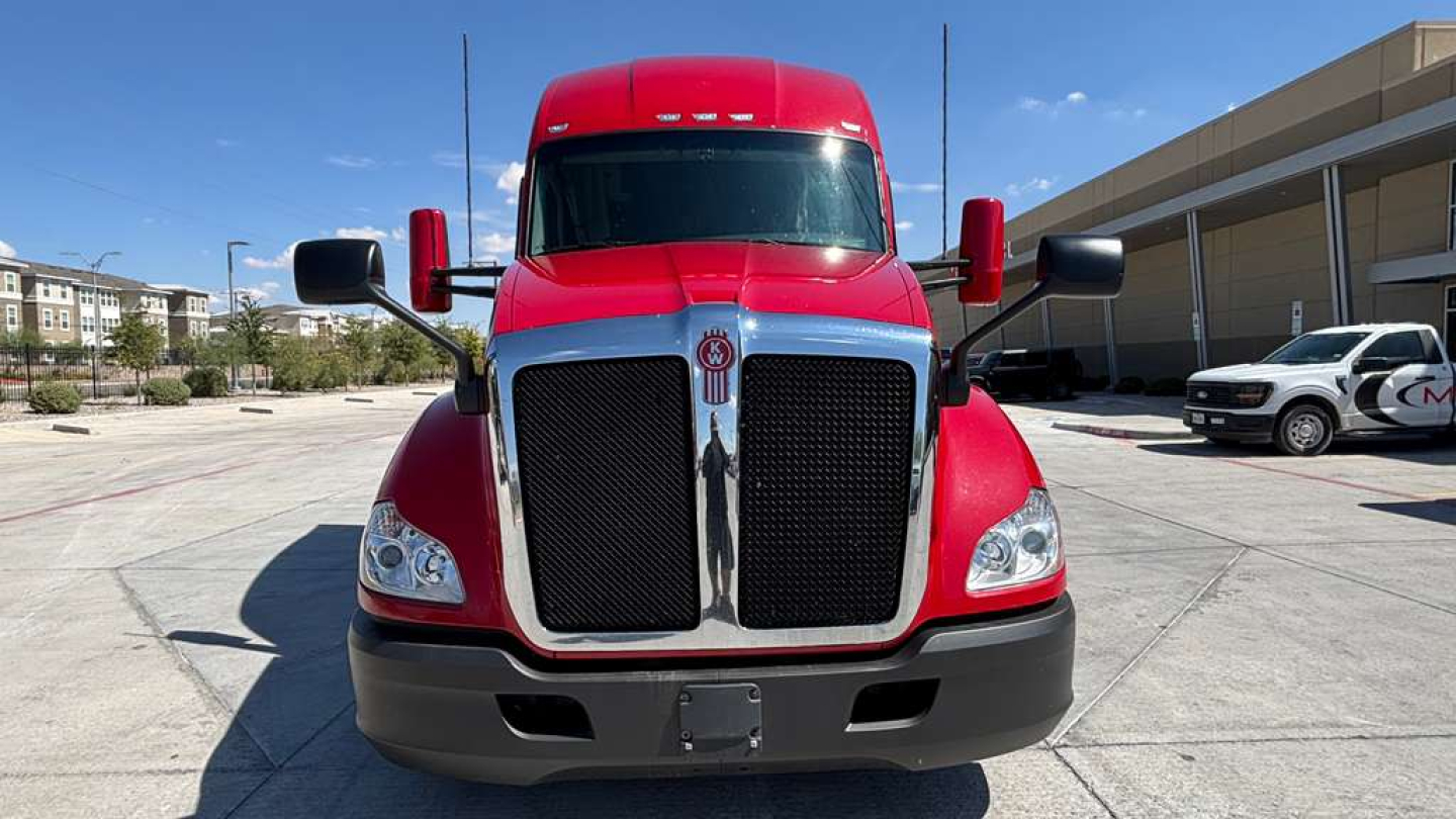 Kenworth T680 front view showing bold black grille, red cab, and large mirrors; daytime outdoor lot; chrome grille surround and bumper area visible.